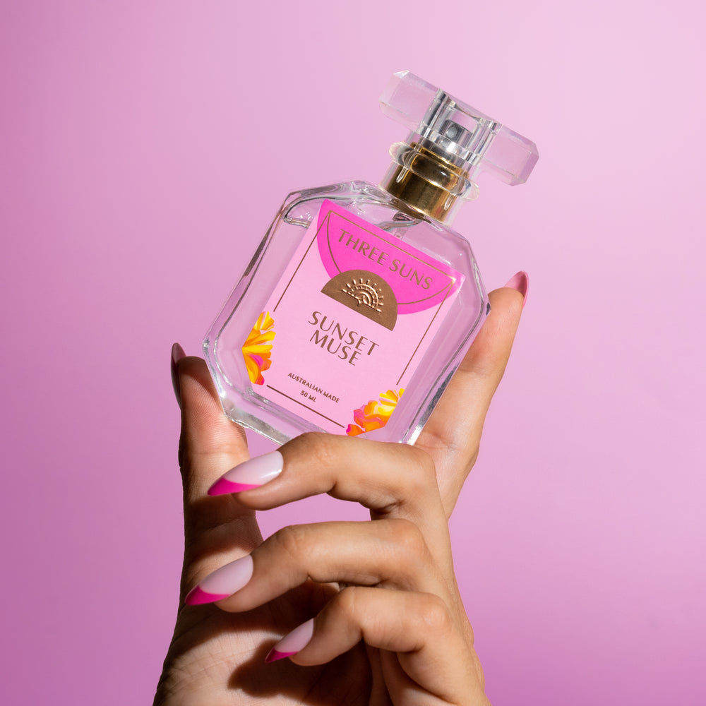 
                      
                        Sunset Muse luxury perfume bottle with gold spray lid, three suns label, and candle gift set on neutral background
                      
                    